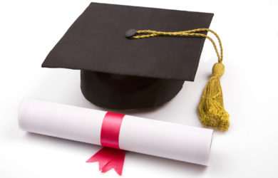 A graduation cap with a gold tassel is placed next to a rolled diploma tied with a red ribbon on a white surface.