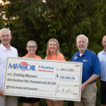 MFA Oil CEO Jon Ihler, and others stand outdoors holding a large check for $150,000 made out to Feeding Missouri from MFA Oil, Break Time, and Big O Tires, dated June 2, 2025. They are smiling with greenery in the background.
