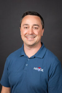 Adam Buckallew, MFA Oil's Member Relations Manager, wearing a blue polo shirt with an MFA Oil logo, smiles against a dark background.