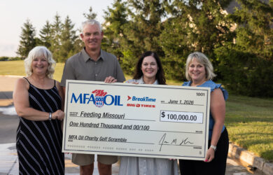 Four people stand outdoors holding a large ceremonial check for $100,000 made out to Feeding Missouri from MFA Oil Charity Golf Scramble, dated June 1, 2026. Trees and sunlight are visible in the background.