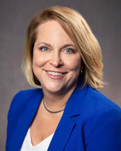 Portrait of Amanda Cooper Chief Human Resources officer a smiling woman with shoulder-length blonde hair, wearing a bright blue blazer over a white top against a neutral background.