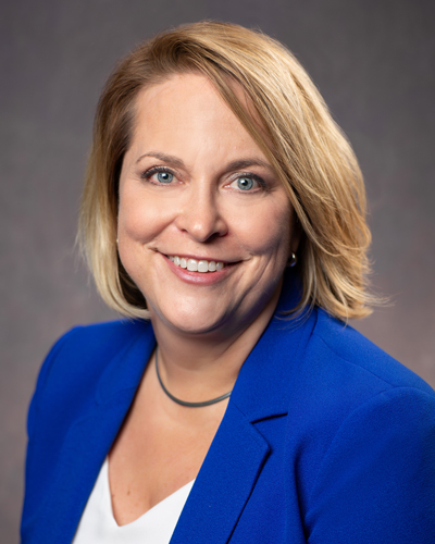 Portrait of Amanda Cooper Chief Human Resources officer a smiling woman with shoulder-length blonde hair, wearing a bright blue blazer over a white top against a neutral background.