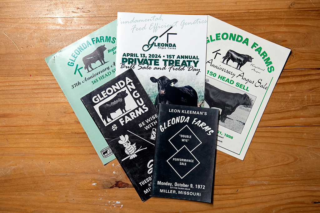 3. Several brochures from Gleonda Angus Farms are spread out on a wooden surface. They advertise events related to cattle sales, dated April 13, 2024, and October 9, 1972, featuring images of Angus cattle.