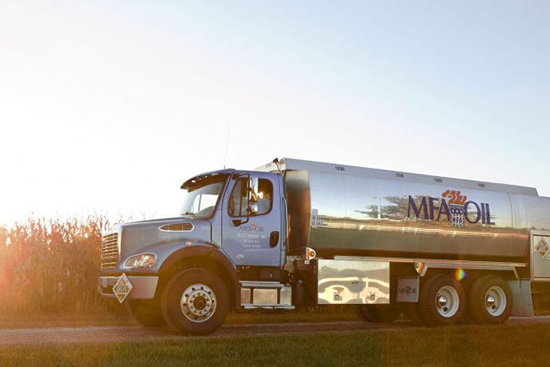 A silver MFA Oil tanker truck is parked on a rural road beside a cornfield at sunset, the iconic MFA Oil logo clearly visible on the side of the vehicle.