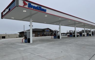 A BreakTime gas station with a canopy and multiple fuel pumps. The station is situated on a concrete lot with a convenience store in the background. The sky is overcast.