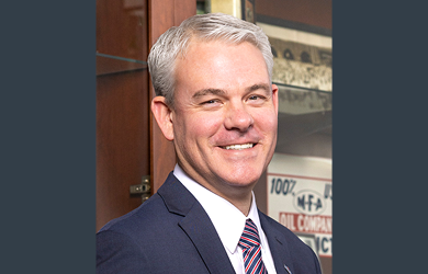 MFA Oil President and CEO Jon Ihler is standing in front of a wooden display cabinet.