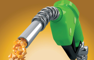 A green fuel pump nozzle dispensing kernels of corn, symbolizing biofuel. The background is a gradient of brown and orange.