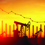 Silhouetted oil pumpjacks in a field at sunset with a descending graph line overlaid, indicating a decrease in oil production or prices.