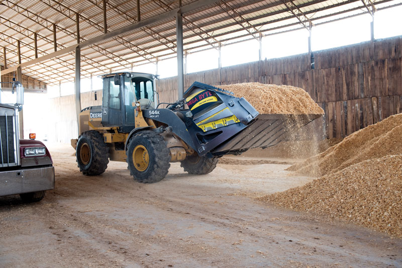 A worker scoops up pine shavings with a loader equipped with a 7.5-cubic-yard bucket.