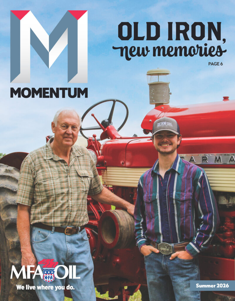 Two men stand in front of a red vintage Farmall tractor, smiling. The older man wears a light blue shirt; the younger wears a plaid shirt and cap. Magazine text reads OLD IRON, new memories and MFA OIL.