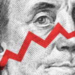 Close-up of a Benjamin Franklin portrait from a U.S. hundred-dollar bill, overlaid with a red zigzag line resembling an upward stock market graph, symbolizing resilience despite recessionary pressures.