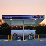 A rural gas station at sunset with an MFA Oil sign and two fuel pumps on a gravel lot. Trees are visible in the background.