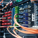 Close-up of a network server with multiple colored cables connected. The image shows intricate wiring and connectors, highlighting data transmission and technology infrastructure.