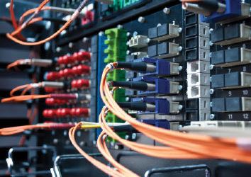 Close-up of a network server with multiple colored cables connected. The image shows intricate wiring and connectors, highlighting data transmission and technology infrastructure.